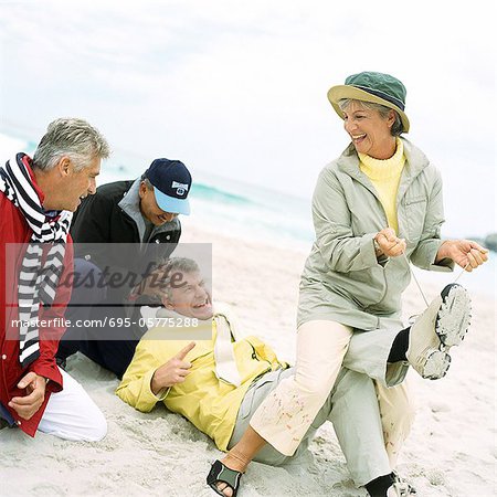 Mature groupe jouant sur la plage, femme, tirant les lacets de l'homme