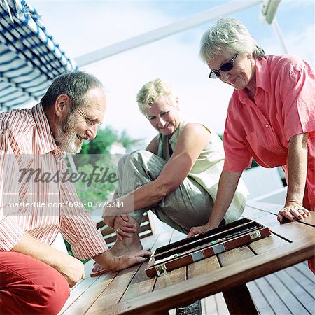 Three mature adults playing backgammon