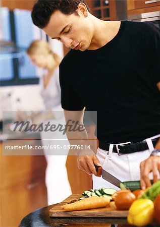 Man slicing vegetables in kitchen, mid-section