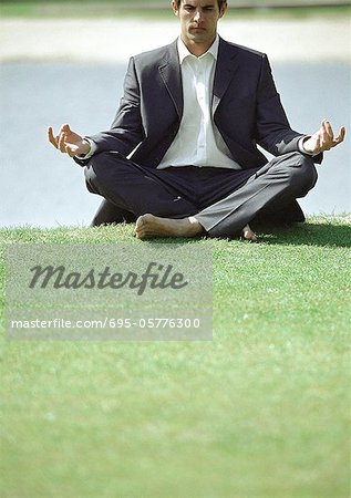 Homme d'affaires en position du lotus sur l'herbe