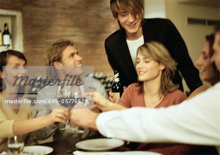 Group of young people around table, clinking glasses