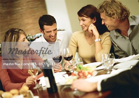 Group of young people around table, drinking wine and laughing