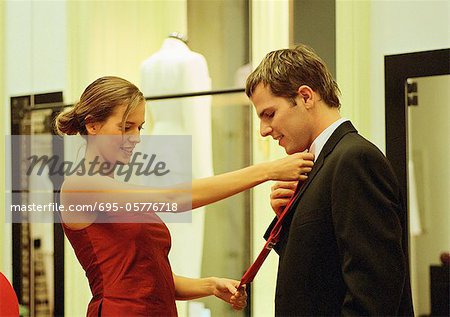 Woman holding neck tie up to man's neck in clothing store, side view.