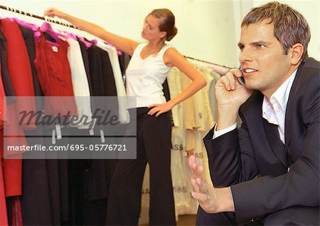 Femme regardant les vêtements en magasin derrière l'homme au téléphone cellulaire.