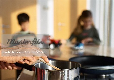 Father cooking in kitchen, children playing at table in background.