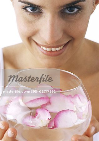 Woman holding bowl of rose petals floating in water, looking at camera, close-up