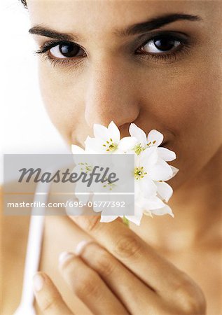 Woman holding white flowers to nose, looking at camera, close-up