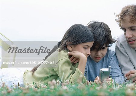 Boy and girl with father lying on stomachs on grass looking at cellphone