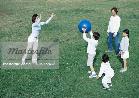 Parents with boys and girl playing ball on grass, full length