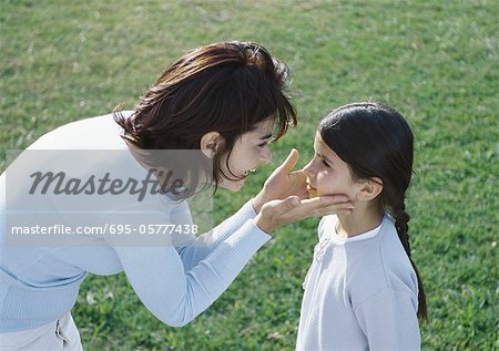 Woman bending over holding daughters face between hands, side view