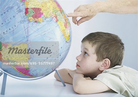 Boy looking at globe, elderly person's hand pointing to spot on globe