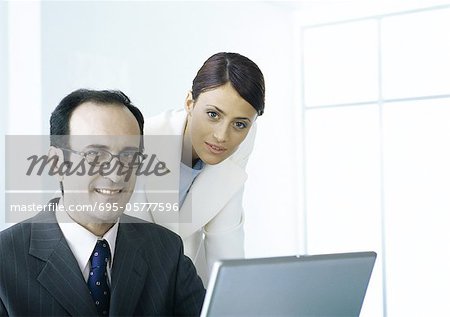 Businessman and businesswoman with laptop looking at camera