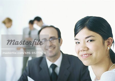 Businesspeople smiling at camera, in background businesspeople taking coffee break