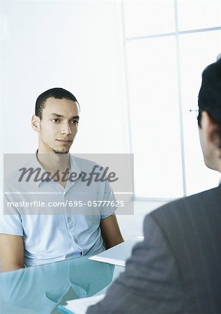 Man in short sleeves with serious expression sitting across table from man in suit