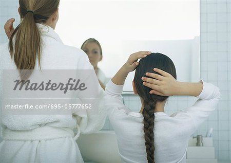 Woman and girl fixing hair, rear view