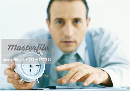 Man holding out alarm clock, focus on hands and clock in foreground