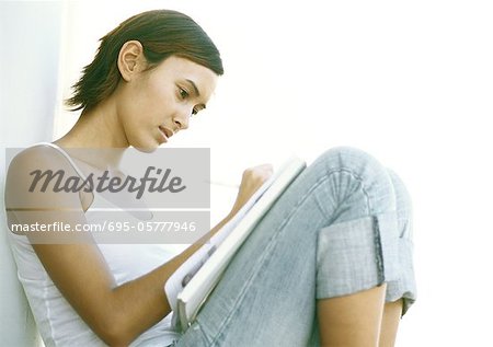 Teenage girl sitting with knees up, writing, side view