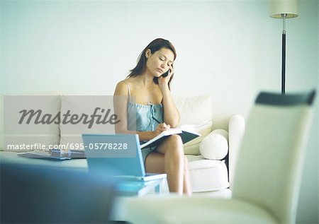 Femme assise sur le canapé avec le téléphone portable à l'oreille, prise de notes