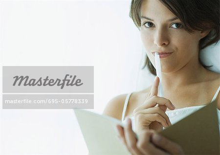 Young woman with pen to lips, holding notebook