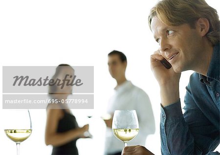 Homme à l'aide de téléphone portable, les gens boire du vin à l'arrière-plan