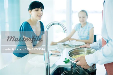 Man draining pasta while woman and girl watch