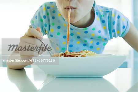 Girl eating spaghetti with tomato sauce, cropped view