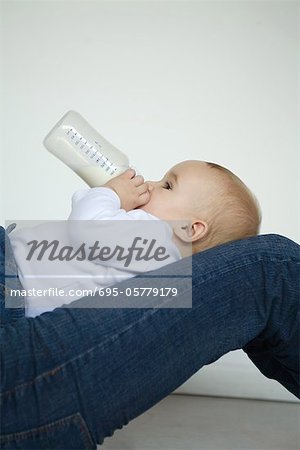 Baby reclining on lap, drinking milk from bottle, side view