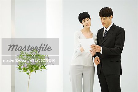 Male and female business partners standing side by side, discussing document