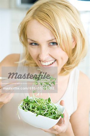 Woman eating radish sprouts with chopsticks, smiling at camera