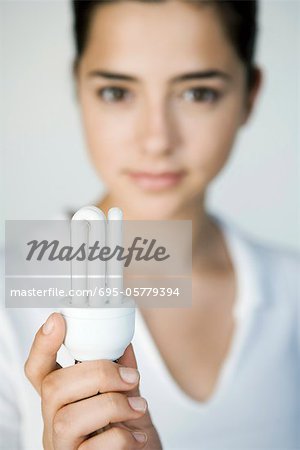 Young woman holding energy efficient light bulb, focus on foreground
