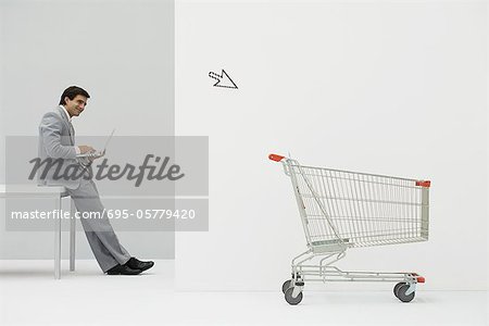 Businessman leaning against desk, shopping online, cursor pointing at shopping cart