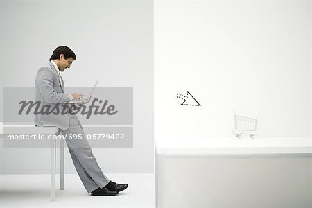 Businessman sitting on desk, shopping online, shopping cart and cursor in foreground