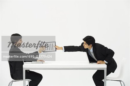 Two business associates sitting face to face at desk, one hand document to the other