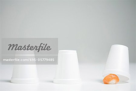 Three disposable cups in row, end cup lifted revealing single piece of nigiri sushi