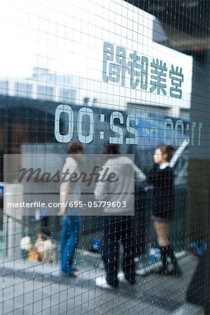 Glass door printed with Japanese text and hours, people standing in background