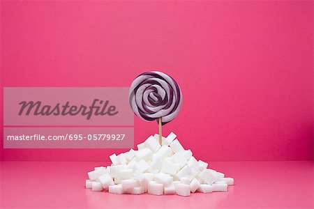 Food concept, lollipop sticking out from pile of sugar cubes Food concept, lollipop sticking out from pile of sugar cubes