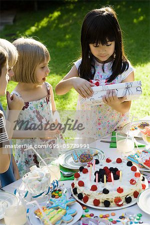 Girl opening gift at birthday party as friends watch