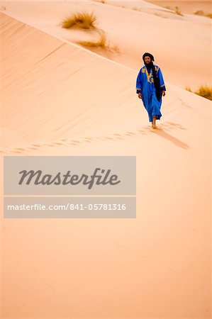 Homme berbère en robe bleue, marchant le long de la crête d'une dune de sable dans la mer de sable de Erg Chebbi près de Merzouga, Maroc, Afrique du Nord, Afrique