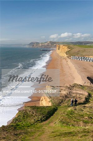 Two walkers enjoy the view along the beautiful vista from the cliffs of Burton Bradstock, looking towards East Cliff, West Bay and Golden Cap, Dorset, England, United Kingdom, Europe