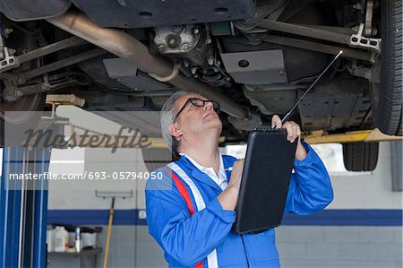 Mechanic scrutinizing the car and writing down something on clipboard