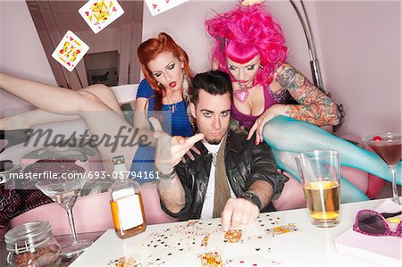 Man tossing playing cards in air with women sitting besides him