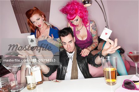 L'homme tenant deux cartes à jouer avec les femmes érotiques assis en dehors de lui