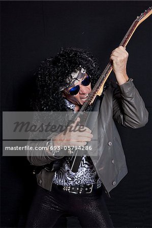 Senior man biting his guitar while performing over black background