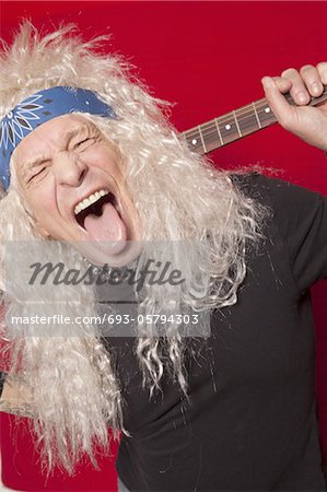 Close-up of middle-aged male guitarist sticking out tongue over colored background