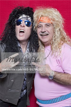 Portrait of musicians gesturing rock music sign over colored background