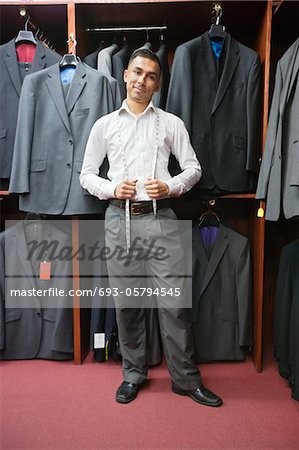 Portrait de jeune homme posant avec costumes suspendus en arrière-plan