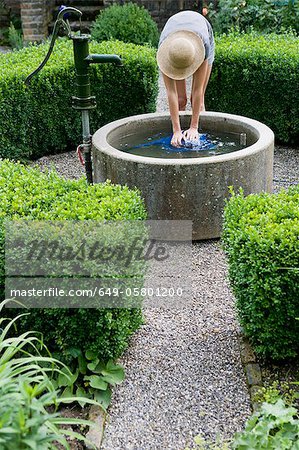 Woman filling watering can in pond