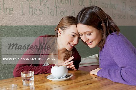 Women whispering to each other in cafe