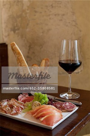 Dish of cold pork meats ,bread sticks and a glass of red wine on a table in a restaurant