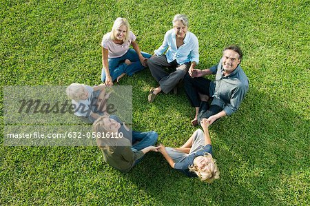 Leute sitzen im Kreis auf Gras, die Hand in Hand, blickte zu Kamera